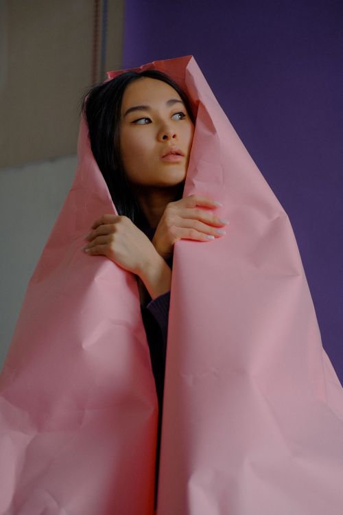 Free A woman wrapped in pink paper gazes thoughtfully, creating a moody portrait with bold colors. Stock Photo