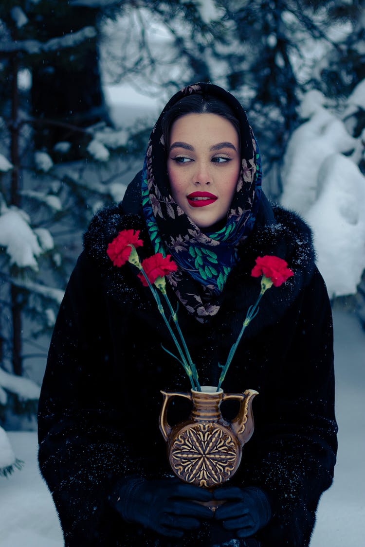 Woman In Winter Clothing Holding A Vase Of Flowers