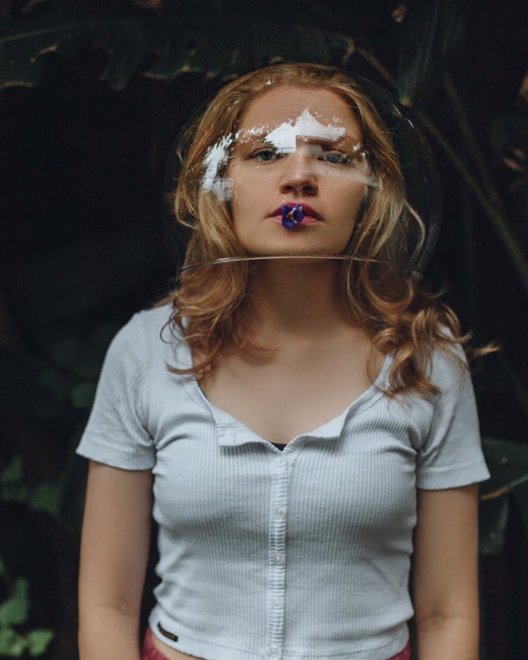 Portrait Of Woman Wearing Glass Bowl On Head Holding Flower In Mouth