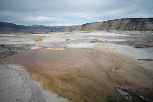 Free Expansive view of geothermal hot springs at Yellowstone with surrounding mountains. Stock Photo
