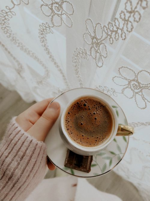 Free A cozy scene of a person holding a coffee cup near a lace curtain. Stock Photo