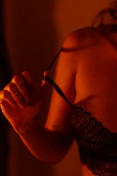 Artistic shot of a woman adjusting her lace lingerie strap with moody lighting.