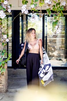 A woman smiling while holding a kiteboard under flowering vines. Ideal for summer sport themes.