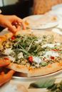 Person Holding Pizza With Green Leaves on Top
