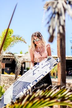 Woman washing kiteboard under outdoor shower in sunny Adicora, Venezuela's vibrant beach scene.