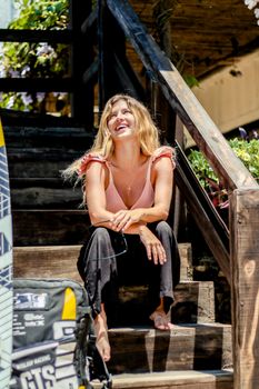 Smiling woman sitting on outdoor wooden steps, enjoying a sunny day in Adicora.