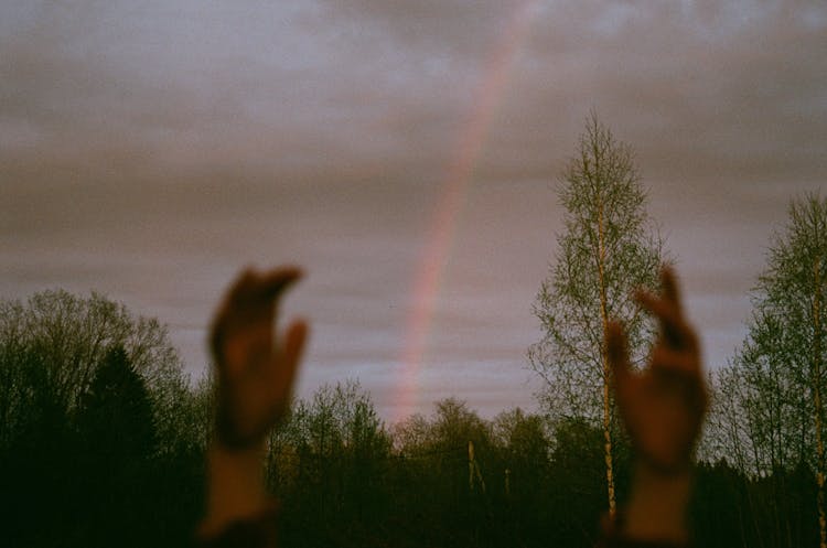 Hands Raised Up Towards Overcast Sky With Rainbow