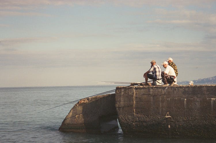 Men Sitting On Concrete Platform Fishing In Sea