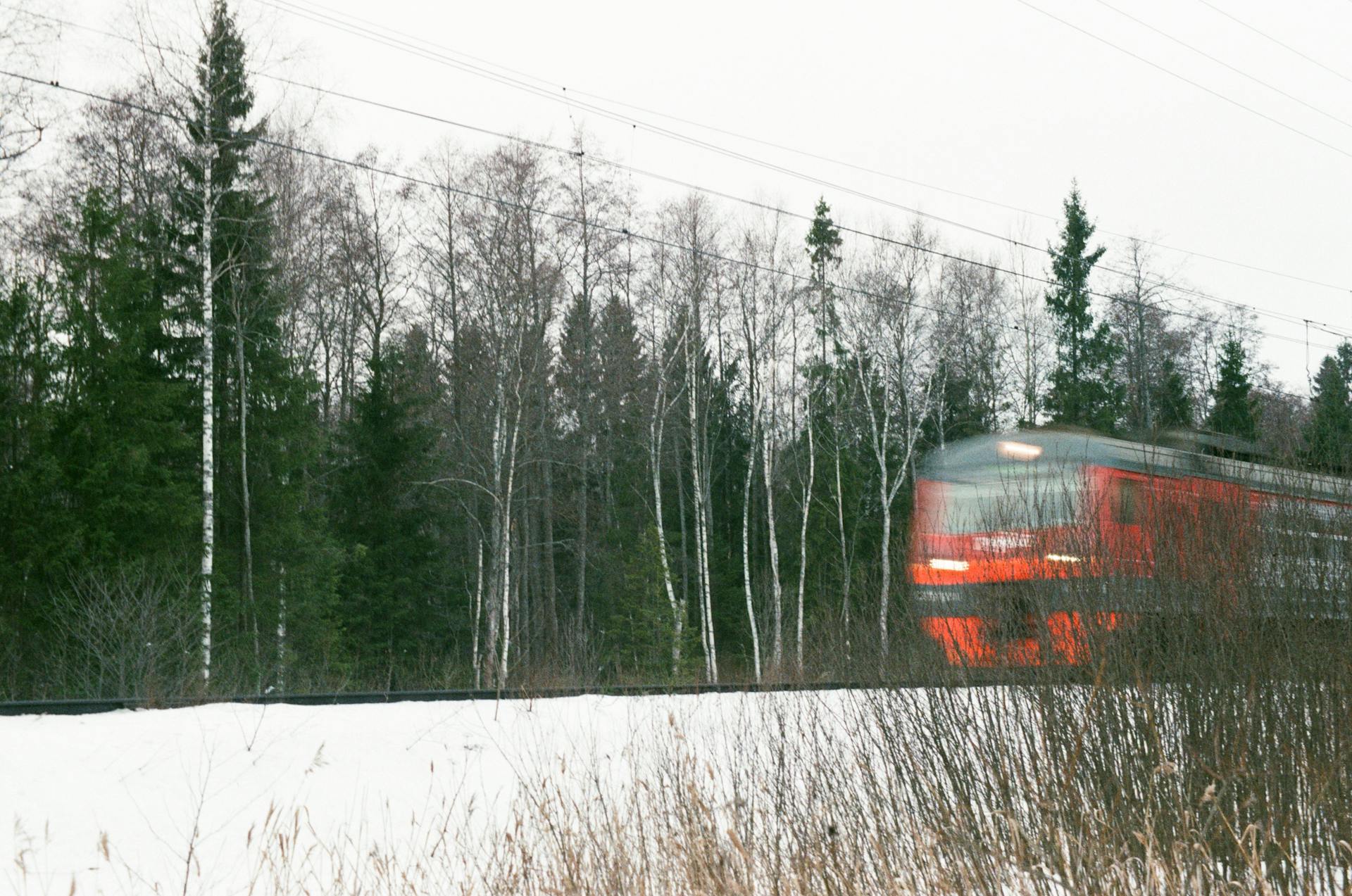 A red train speeds through a snowy landscape in a Russian forest near Taldom, capturing motion blur and winter scenery.