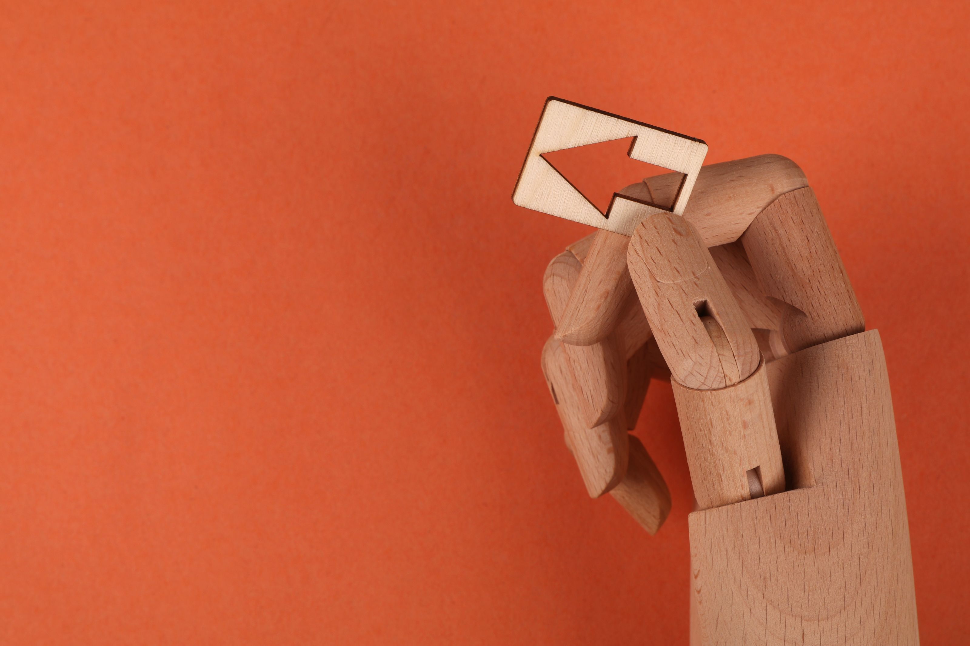 Conceptual image of a wooden mannequin hand holding a wooden arrow against an orange backdrop.
