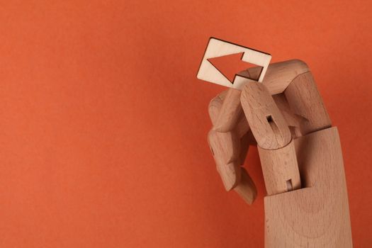 Conceptual image of a wooden mannequin hand holding a wooden arrow against an orange backdrop.