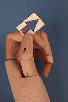 Conceptual image of a wooden hand model holding an arrow symbol against a blue background.