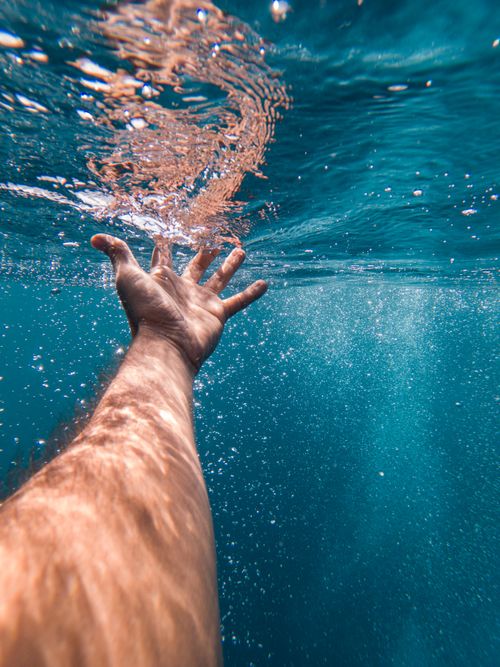 Free A hand reaching up through blue water against sunlight, shot in Zanzibar. Stock Photo