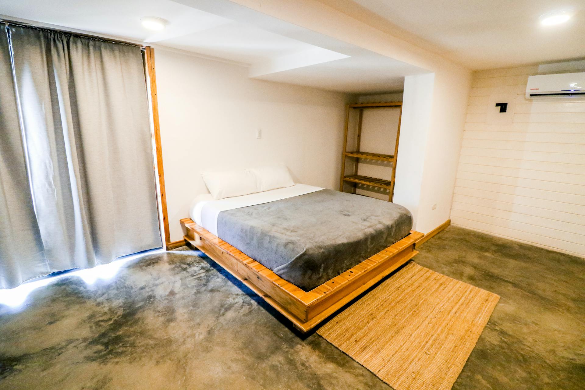 Modern minimalist bedroom with a wooden bed frame and concrete floor in Adicora, Venezuela.