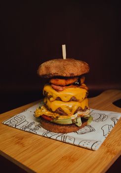 Close-up of a triple cheeseburger with toppings on a wooden board, emphasizing its juicy layers.