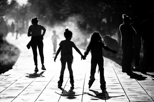 Free Two girls holding hands and roller skating on a sunlit path, creating a playful silhouette. Stock Photo