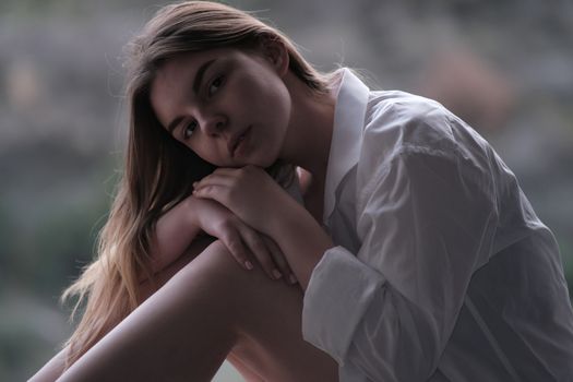 Pensive young woman in white shirt, embracing nature's serenity.