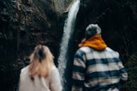 Unrecognizable Couple Looking at Waterfall Coming from Rock