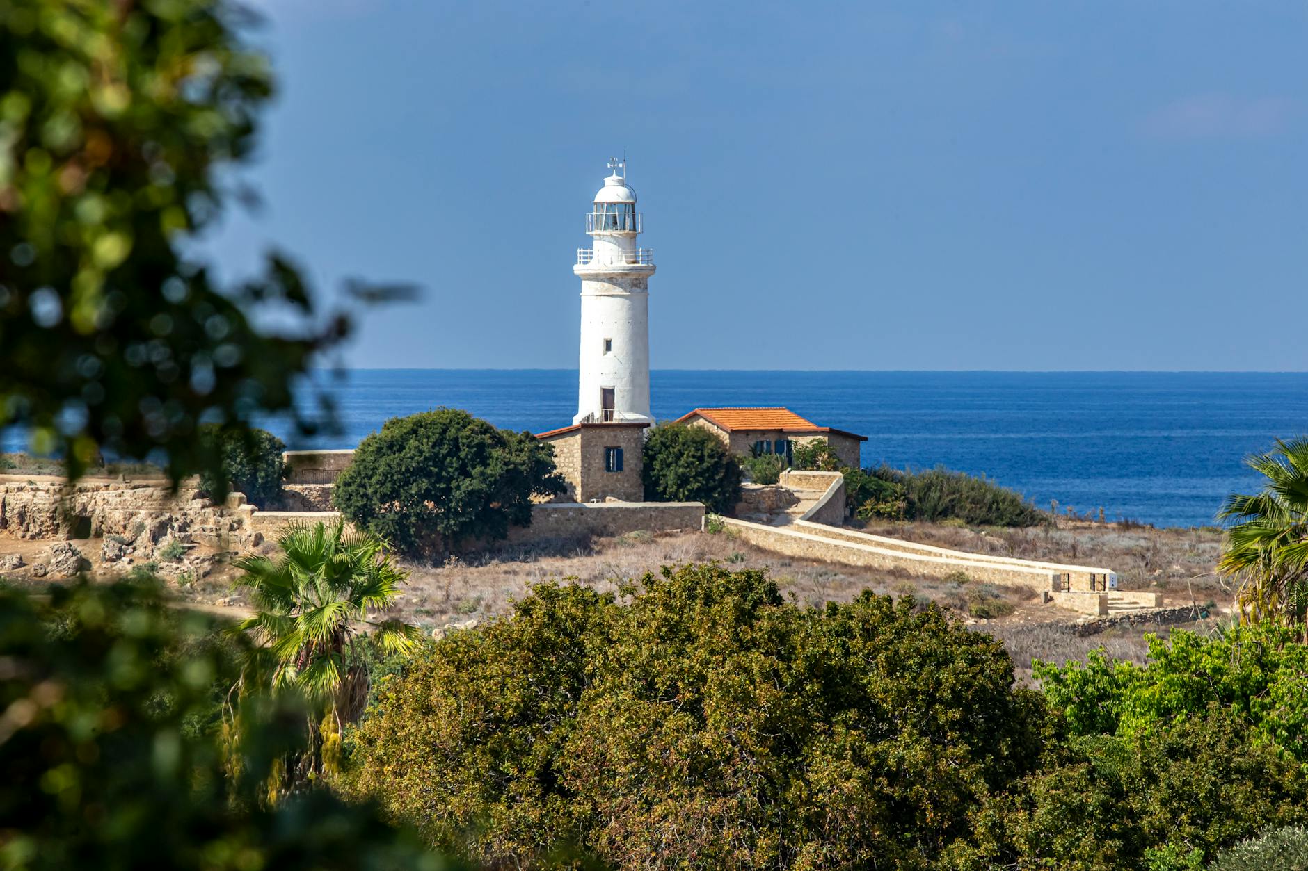 A picturesque lighthouse surrounded by greenery with a sea backdrop.