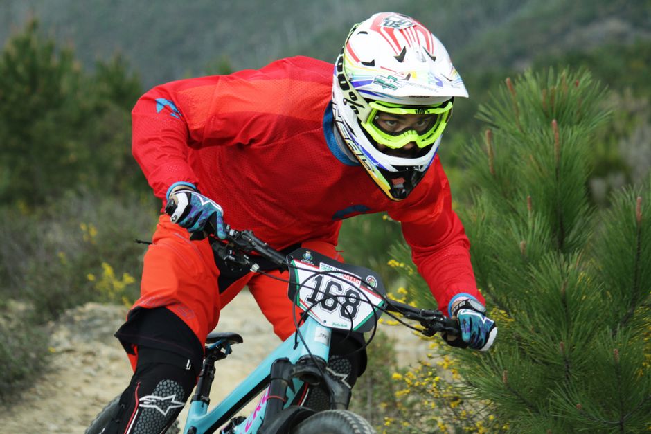 Racer in red gear speeding on a forested mountain trail, showcasing dynamic sports action.