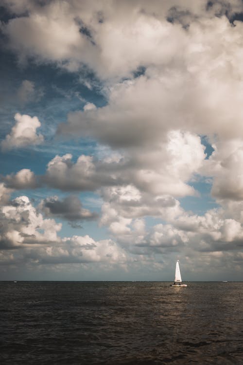 White Sailboat on Sea Under White Clouds and Blue Sky