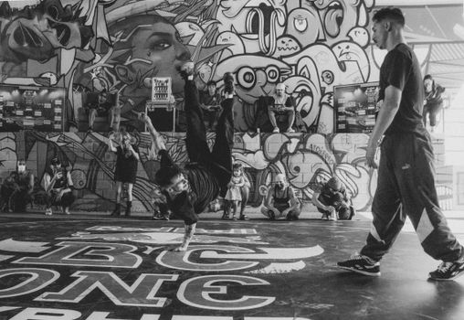 Energetic black and white shot of street dancers performing in front of vibrant graffiti.