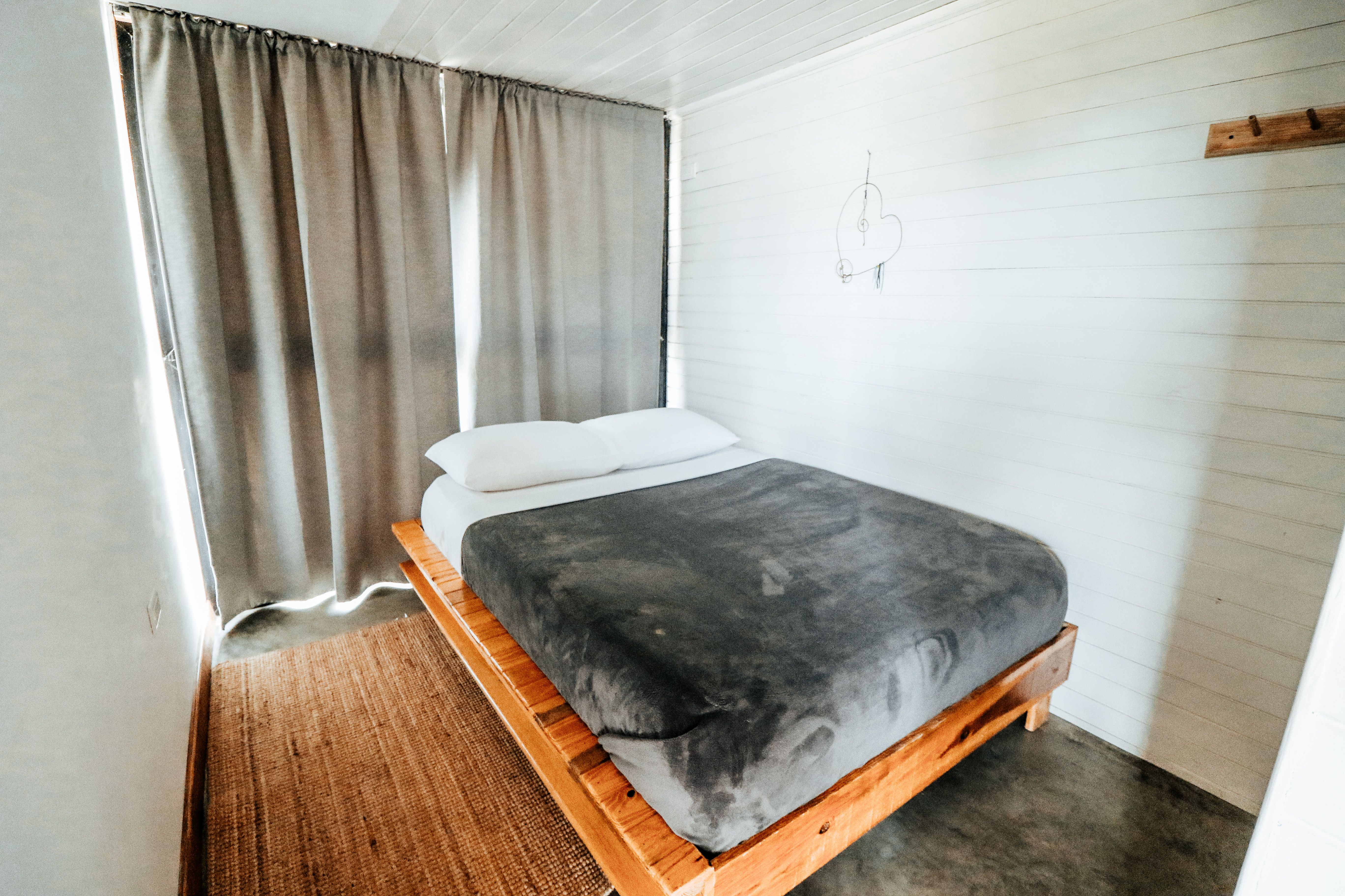 Cama de madeira com colchão, roupa de cama cinza e cortinas claras