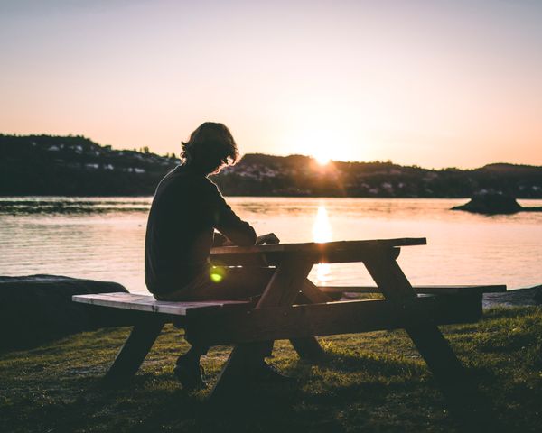 A figure alone on a picnic bench at sunset by the water — Sindre Fs on Pexels