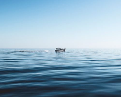 Free A lone boat cruising through calm ocean waters under a clear blue sky. Stock Photo