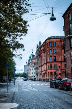 A scenic urban street lined with red brick buildings and cars under an overcast sky.