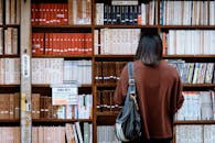 Woman Wearing Brown Shirt Carrying Black Leather Bag on Front of Library Books