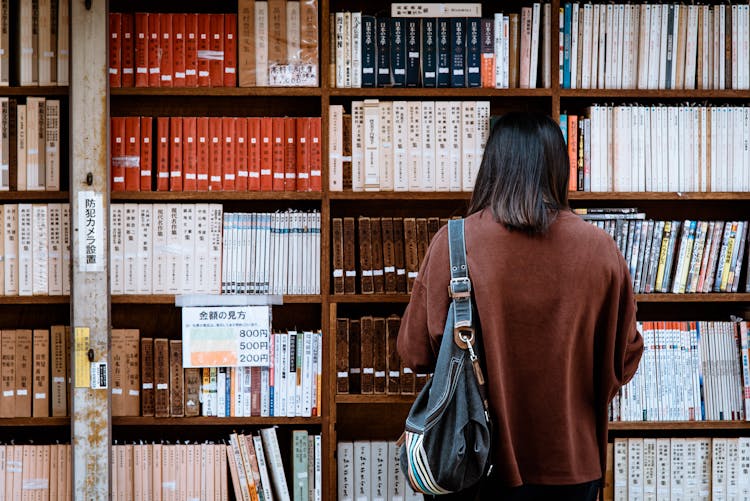 Woman Wearing Brown Shirt Carrying Black Leather Bag On Front Of Library Books