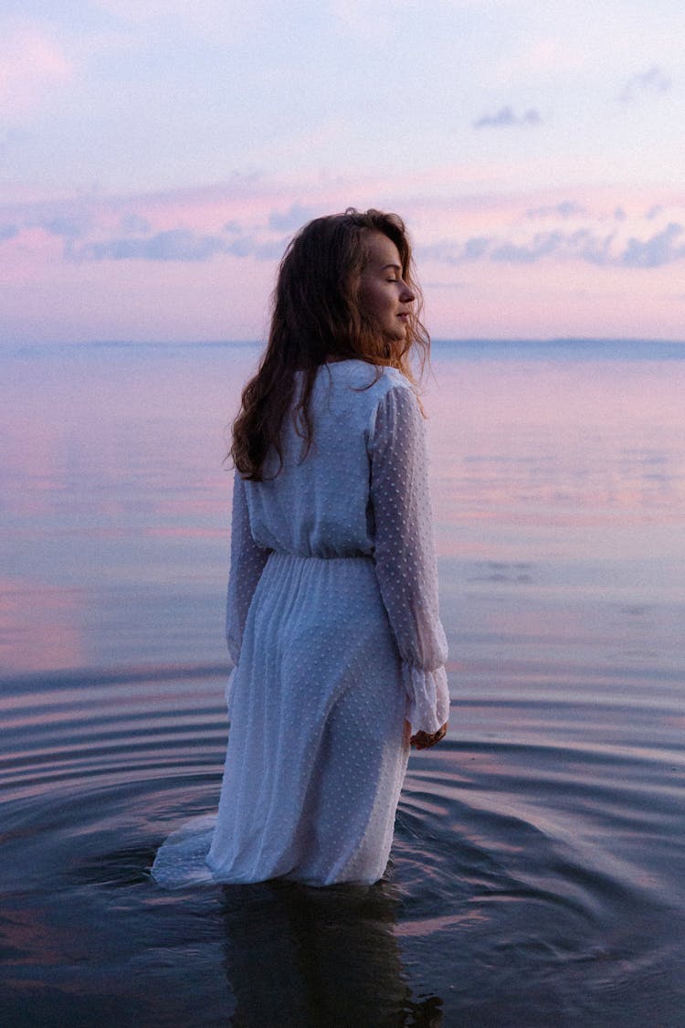 Adult Woman With Long Brown Hair Wearing White Dress And Standing In Lake