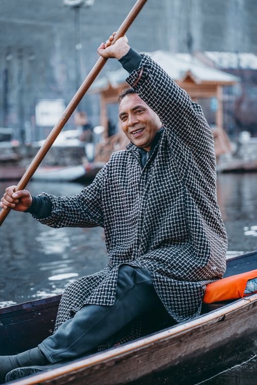 Free Smiling man paddles a wooden boat on serene Srinagar waters. Stock Photo