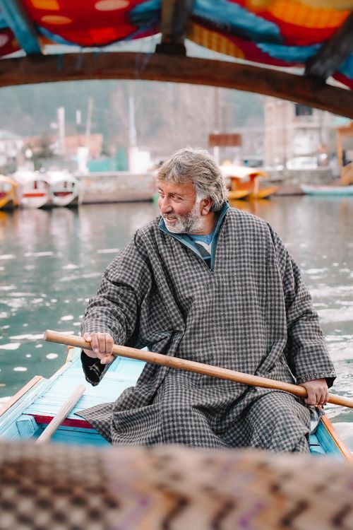 Free A man in traditional attire skillfully rows a wooden boat on a tranquil lake background. Stock Photo