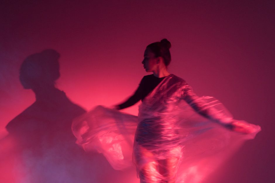 A dancer creates captivating shadows in pink light, showcasing elegance.
