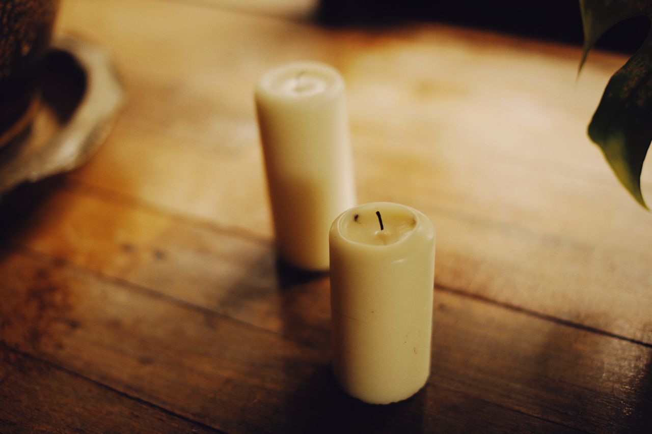 Two cream candles on a wooden table in warm light