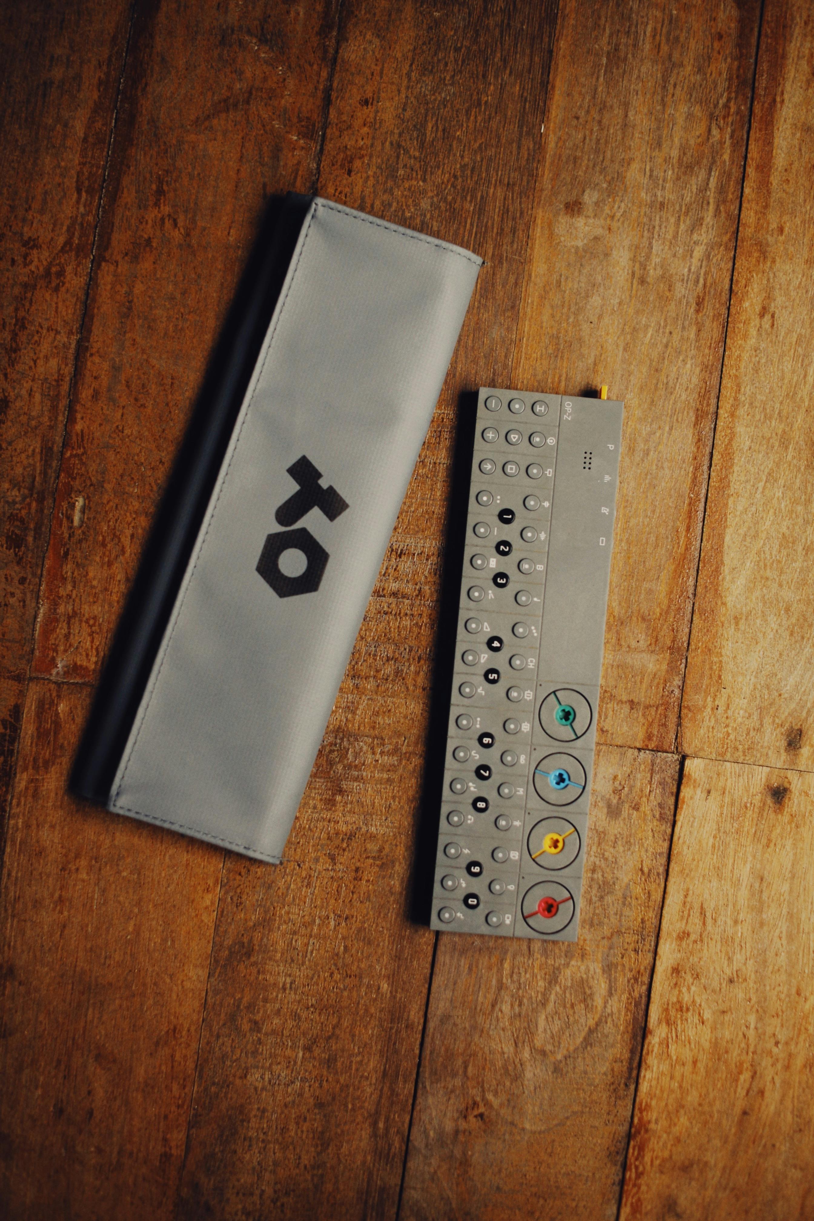 Minimalist design of a compact synthesizer and its case on a wooden floor.