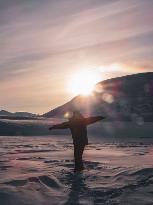 Free A person stands with open arms on a snowy landscape during a captivating sunset, creating a serene winter scene. Stock Photo