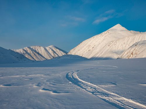 Free Expansive snowy mountains under a clear blue sky with visible snow tracks. Stock Photo