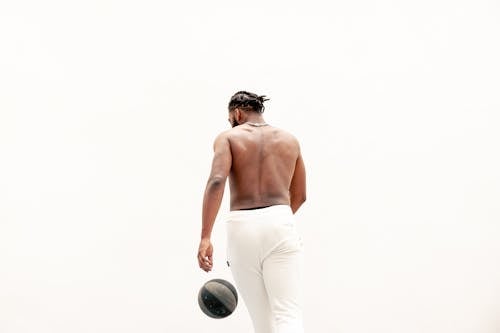 Topless Man in White Pants Playing a Ball