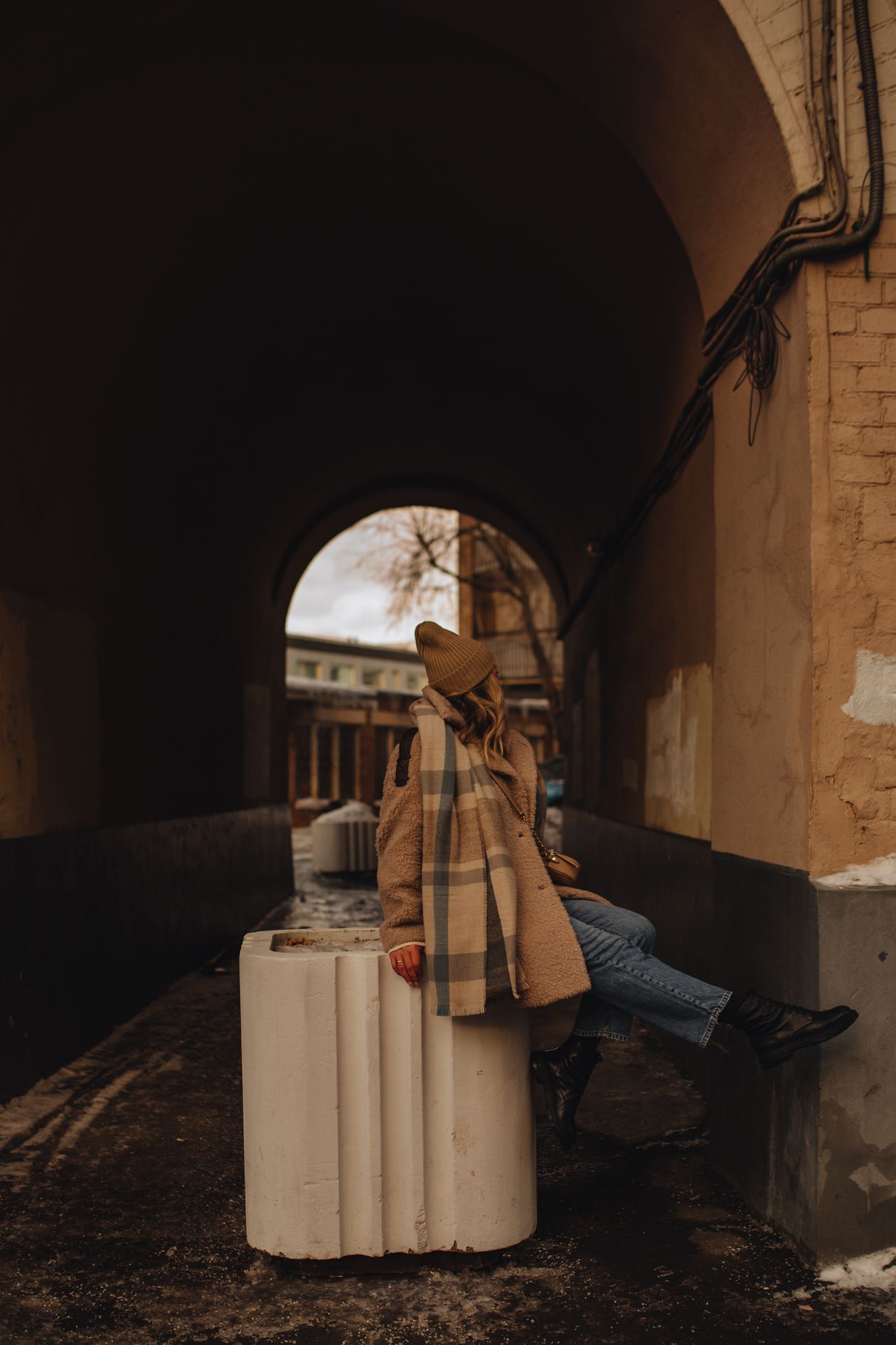 Woman in a teddy coat with blue jeans and black ankle boots in an arched passageway