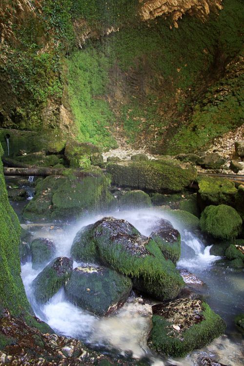 Free Calm cascading waterfall over moss-covered rocks in a tranquil natural canyon setting. Stock Photo