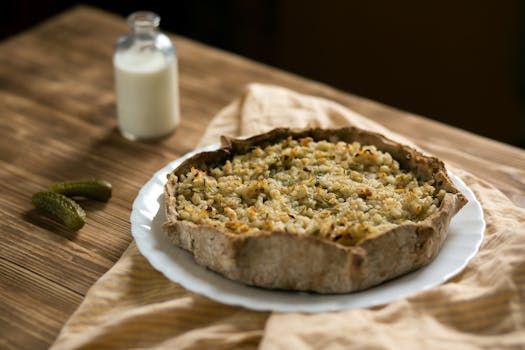 Warm rustic tart on a wooden table with a bottle of milk and pickles.