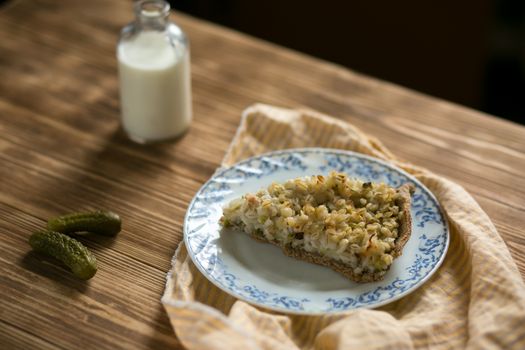 A slice of rustic potato pie on a decorative plate with milk and pickles nearby.