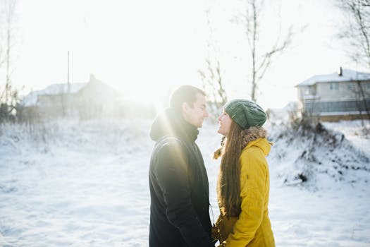 Smiling couple face to face in winter clothing under bright sun on snowy ground.