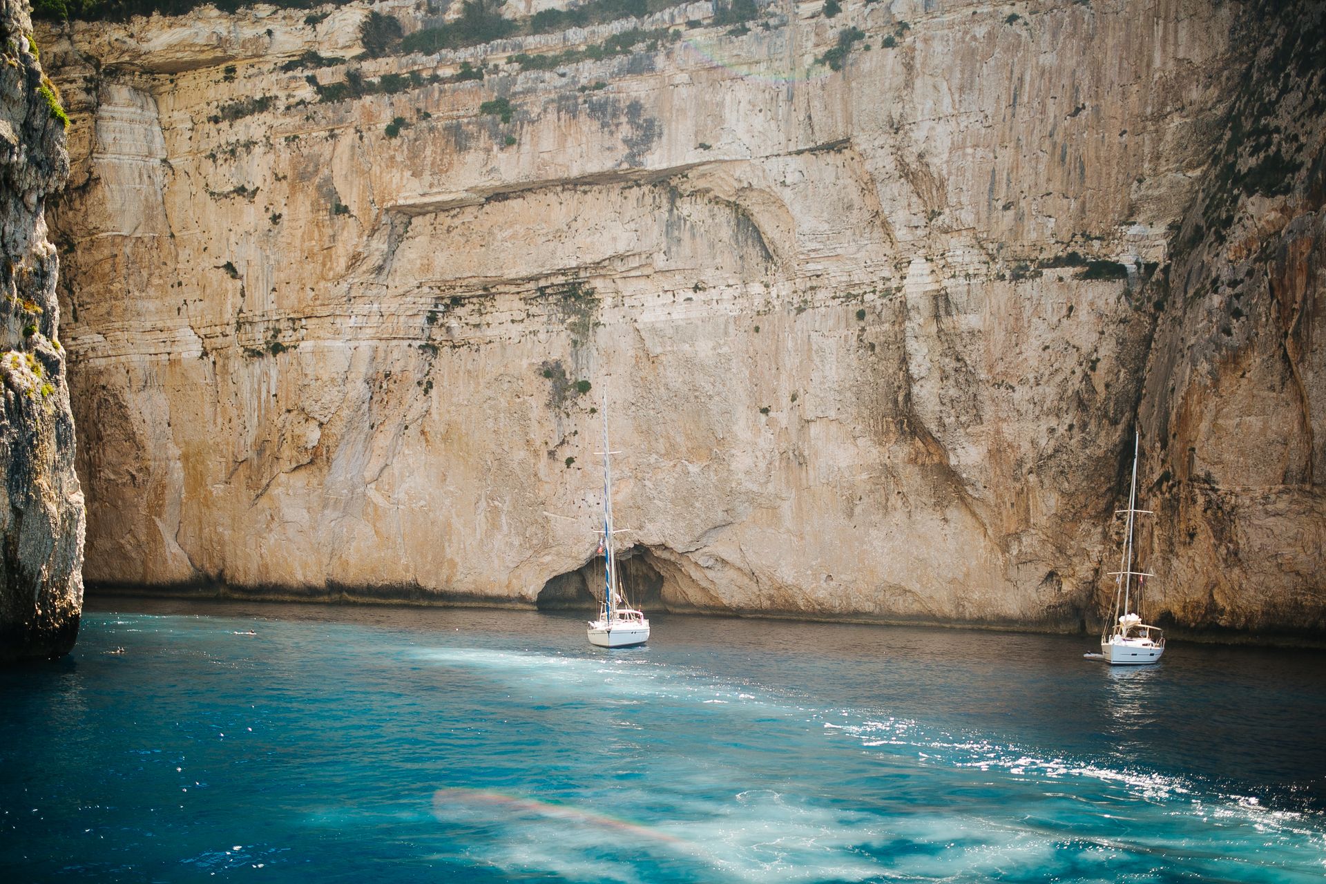 Two sailboats anchored near a striking cliffside, creating a serene nautical scene.