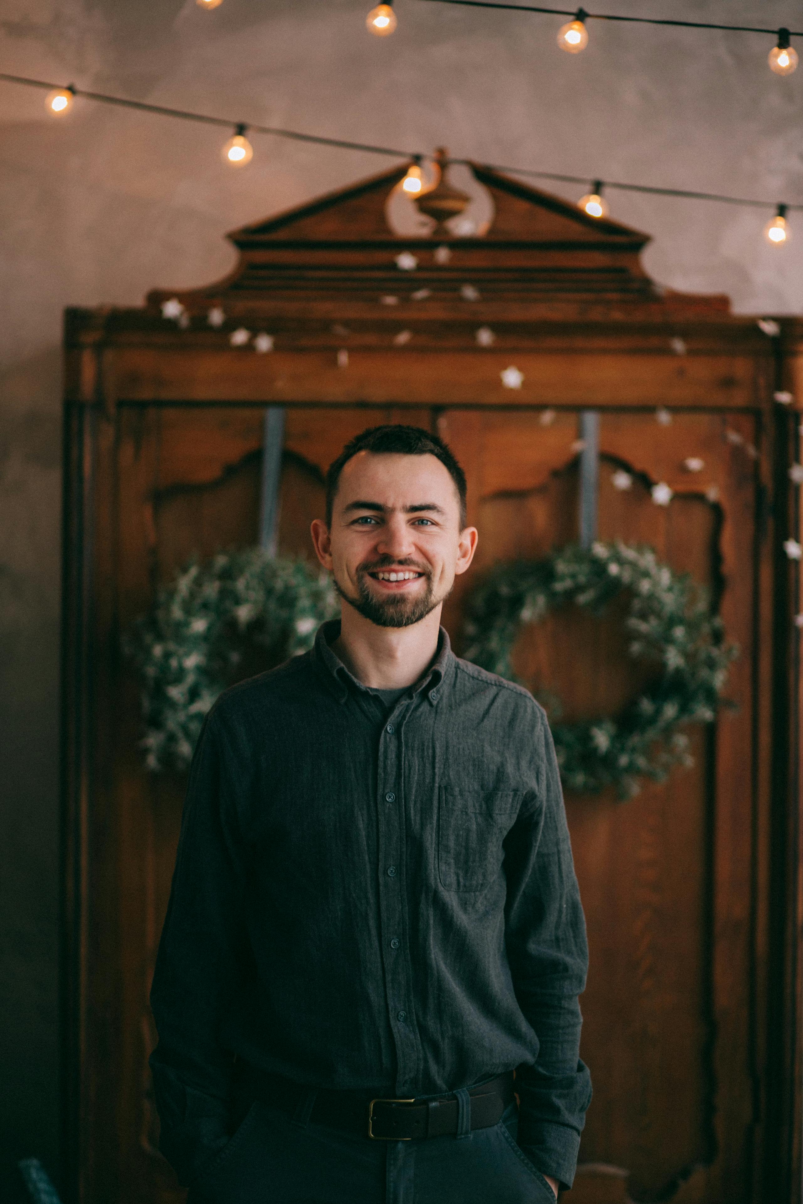 A man smiling in front of a wooden dresser with festive decorations indoors.