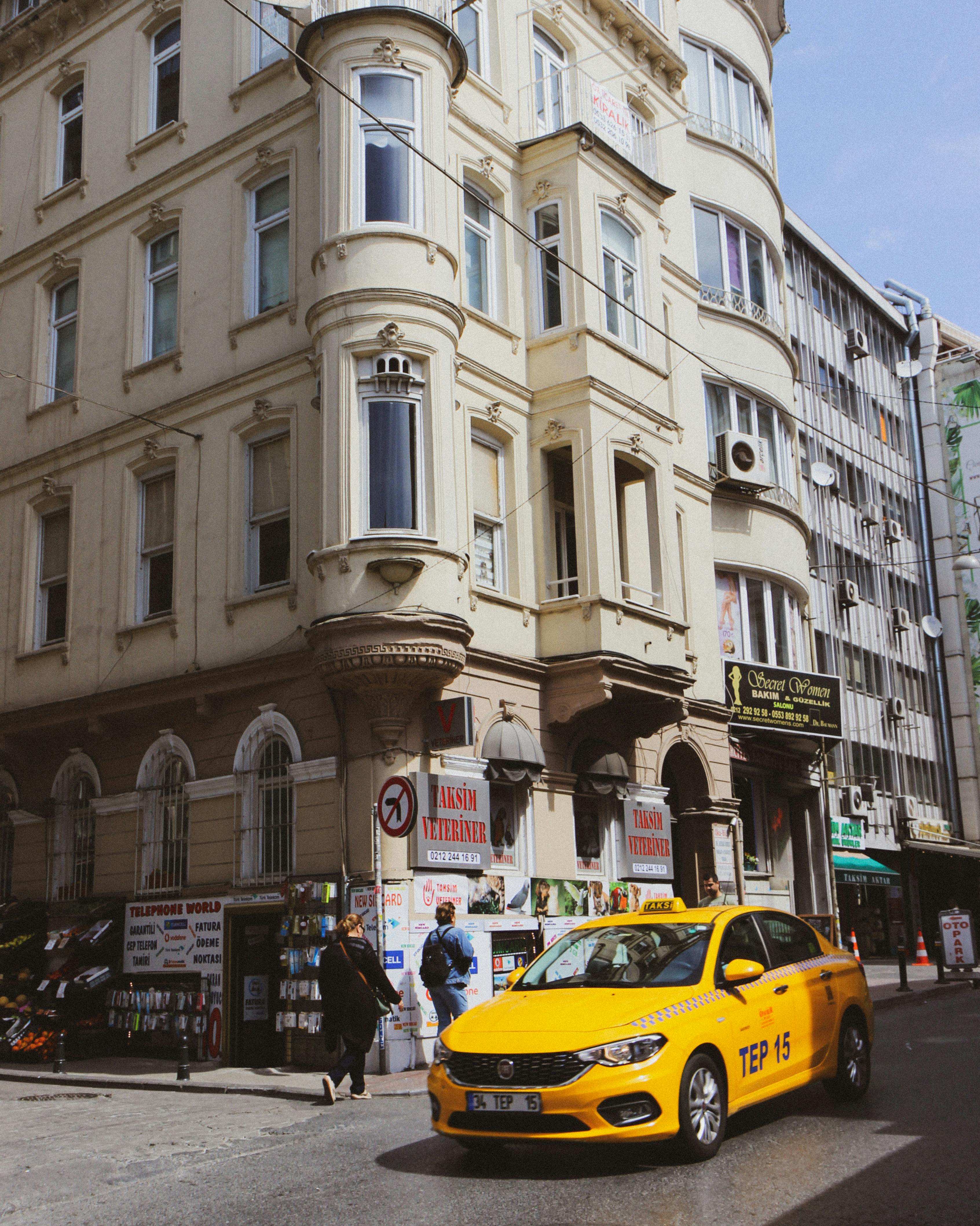 Free A yellow taxi drives past historic European architecture on a sunny day. Stock Photo