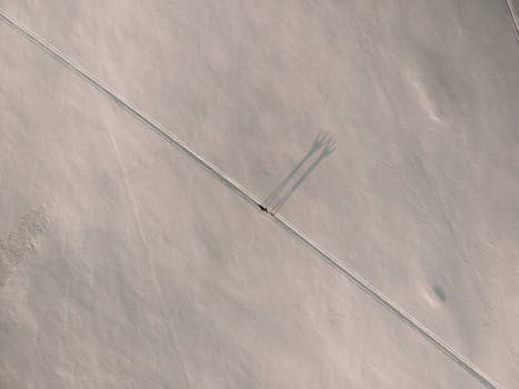 A drone captures a lone vehicle traveling a snowy path in Novosibirsk winter, casting distinct shadows.
